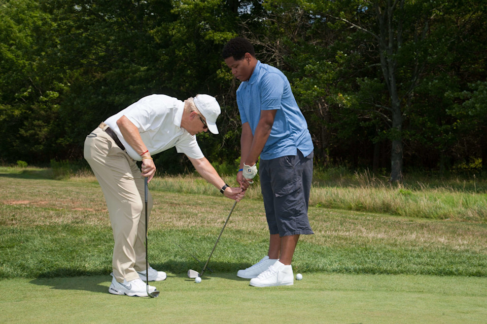 Golf professional giving a private golf lesson on a driving range on how to hit a ball.